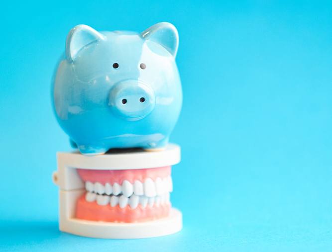 piggy bank atop model teeth representing cost of cosmetic dentistry in West Lake Hills