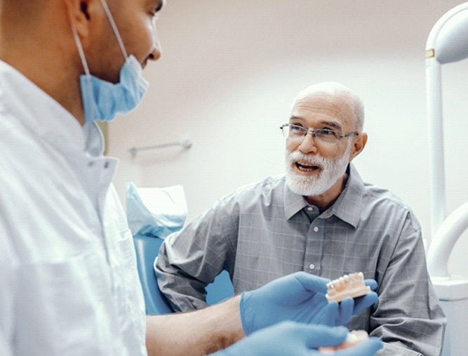 A dentist holds a mouth mold while talking to an older man about the potential for implant dentures