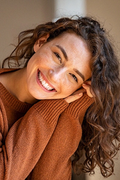 Closeup of woman with healthy, beautiful teeth smiling in brown sweater