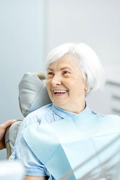 An older woman smiling while listening to her dentist talk about the many benefits she’ll enjoy because of her implant dentures in West Lake Hills