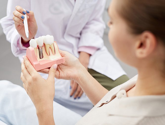 Dentist showing patient a model dental implant supported replacement tooth