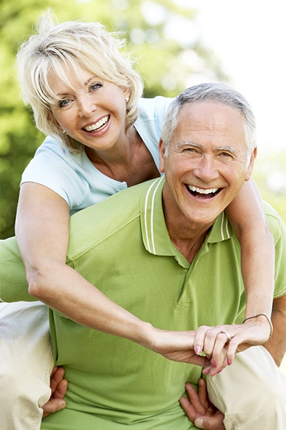 Older man and woman smiling after replacing missing teeth