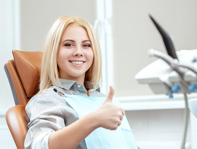 Woman giving thumbs up after dental checkup and teeth cleaning visit