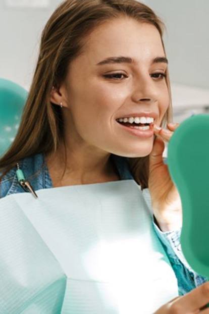 Patient smiling in mirror after successful dental implant salvage