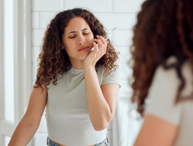 Woman experiencing dental pain while brushing teeth