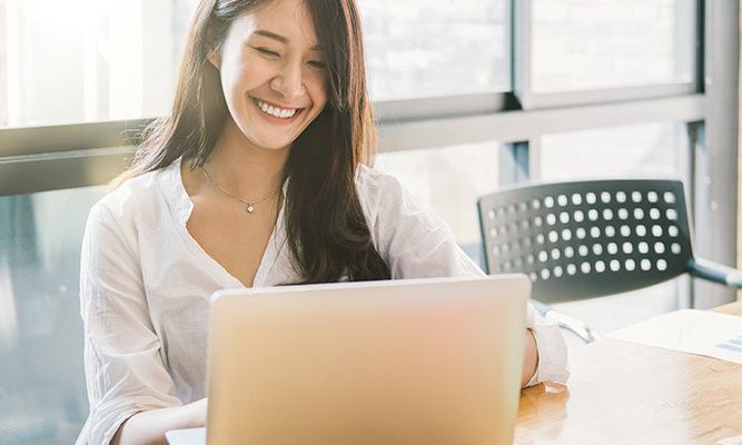 Woman with dark hair smiling and sitting at her laptop