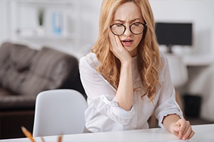 Woman with cracked tooth holding cheek in pain