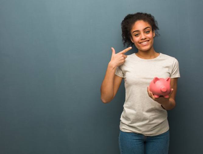 Woman holding a piggy bank and pointing to her smile after a smile makeover in West Lake Hills