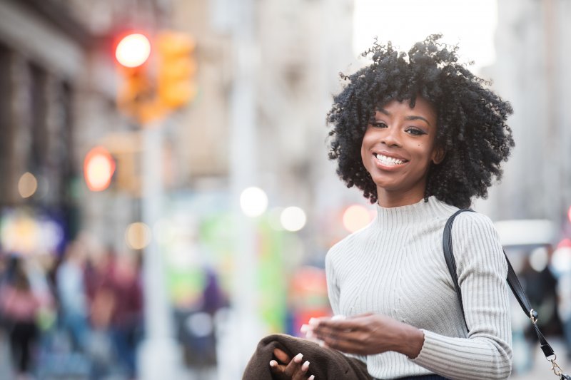 a young woman walking on a street and smiling, showing off her healthy, fully intact smile